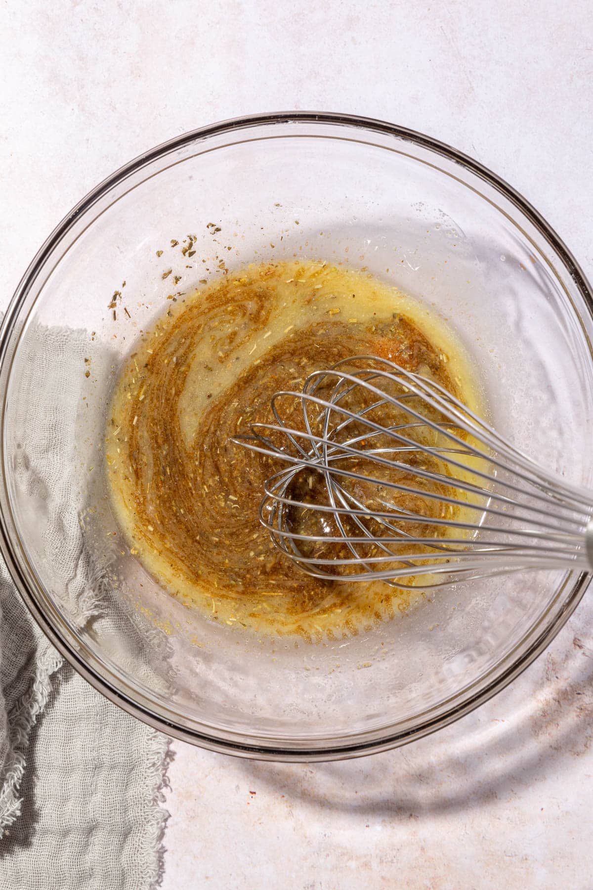 A glass bowl with a melted butter and spice mixture that is being whisked.