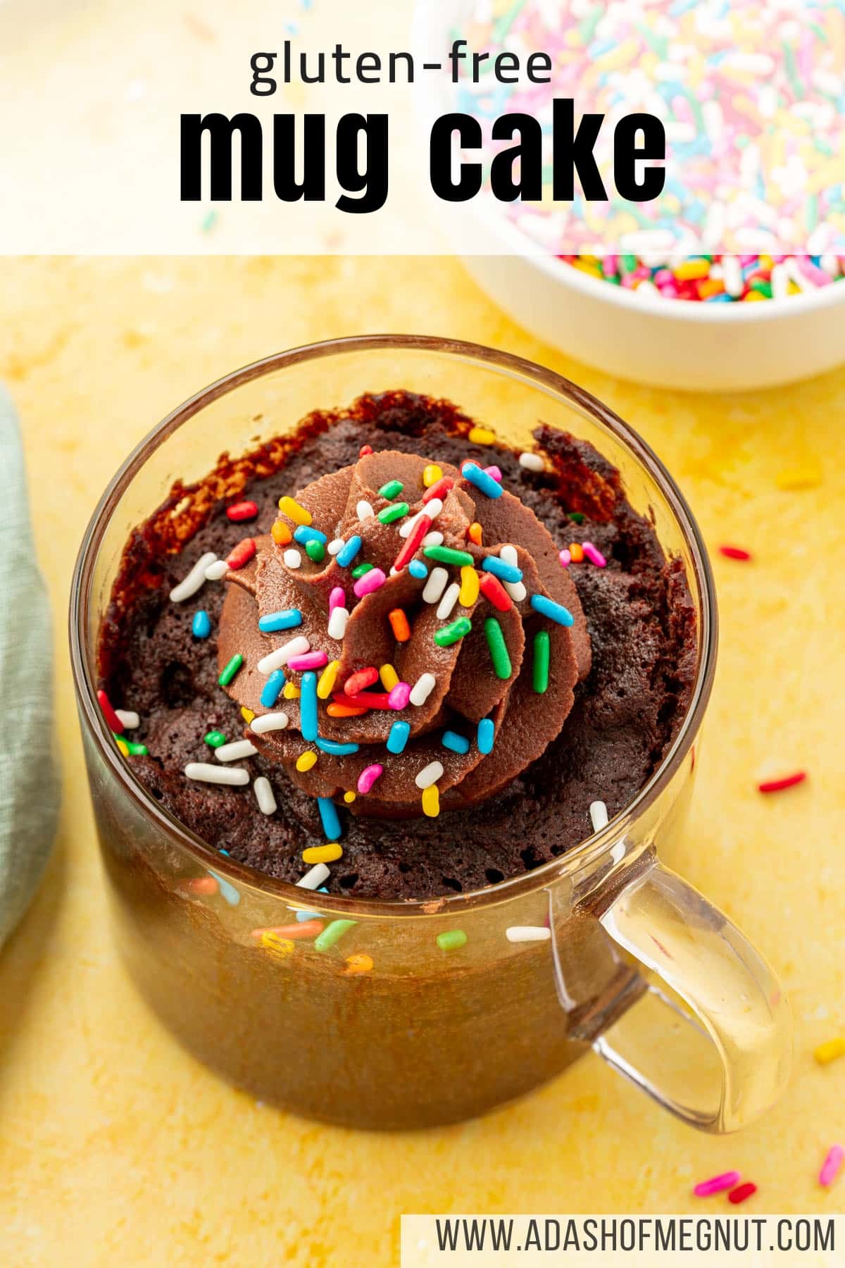 A closeup of a gluten-free mug cake in a glass mug topped with a swirl of chocolate buttercream and colorful sprinkles.