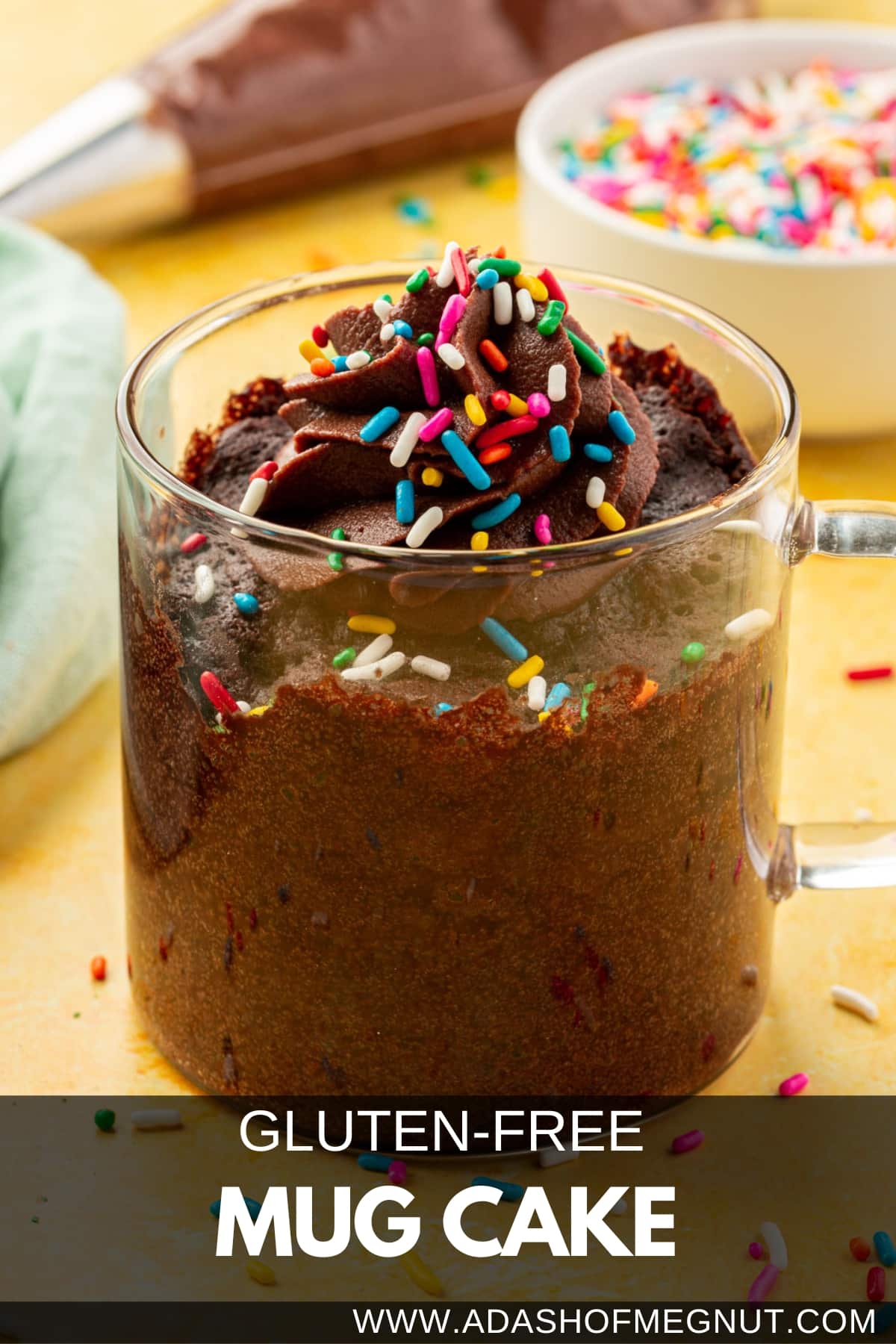 A gluten-free chocolate mug cake in a glass mug topped with chocolate frosting and rainbow sprinkles.