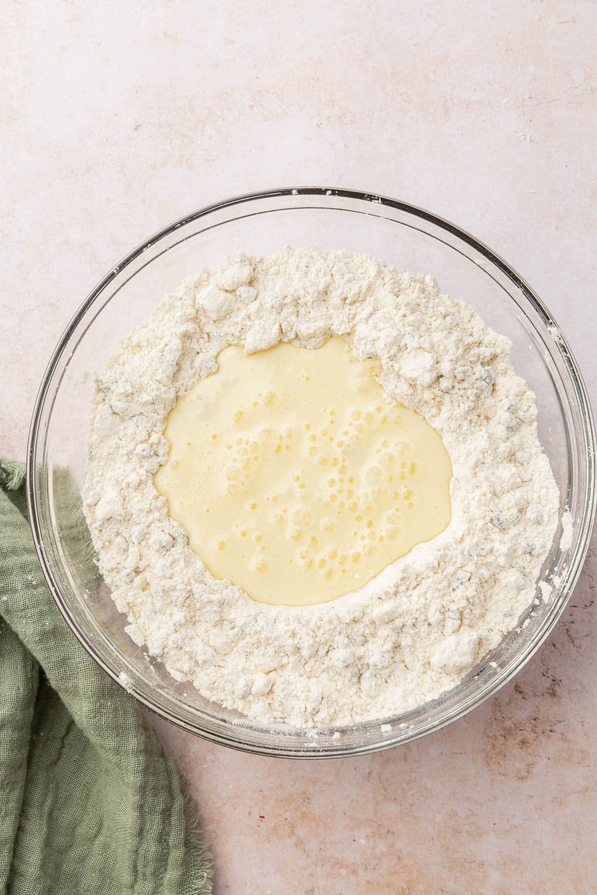 A glass mixing bowl with gluten-free flour blend mix with a buttermilk mixture in the center.