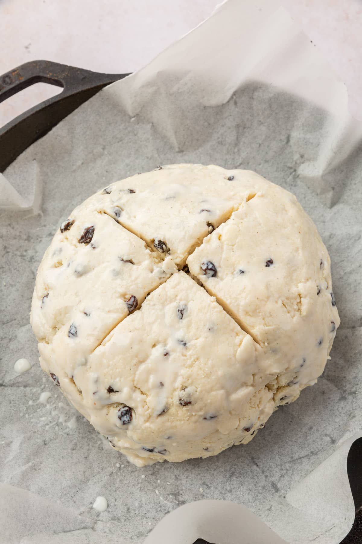 Gluten-free irish soda bread dough in a cast iron skillet lined with parchment paper that has a cross cut into the top.