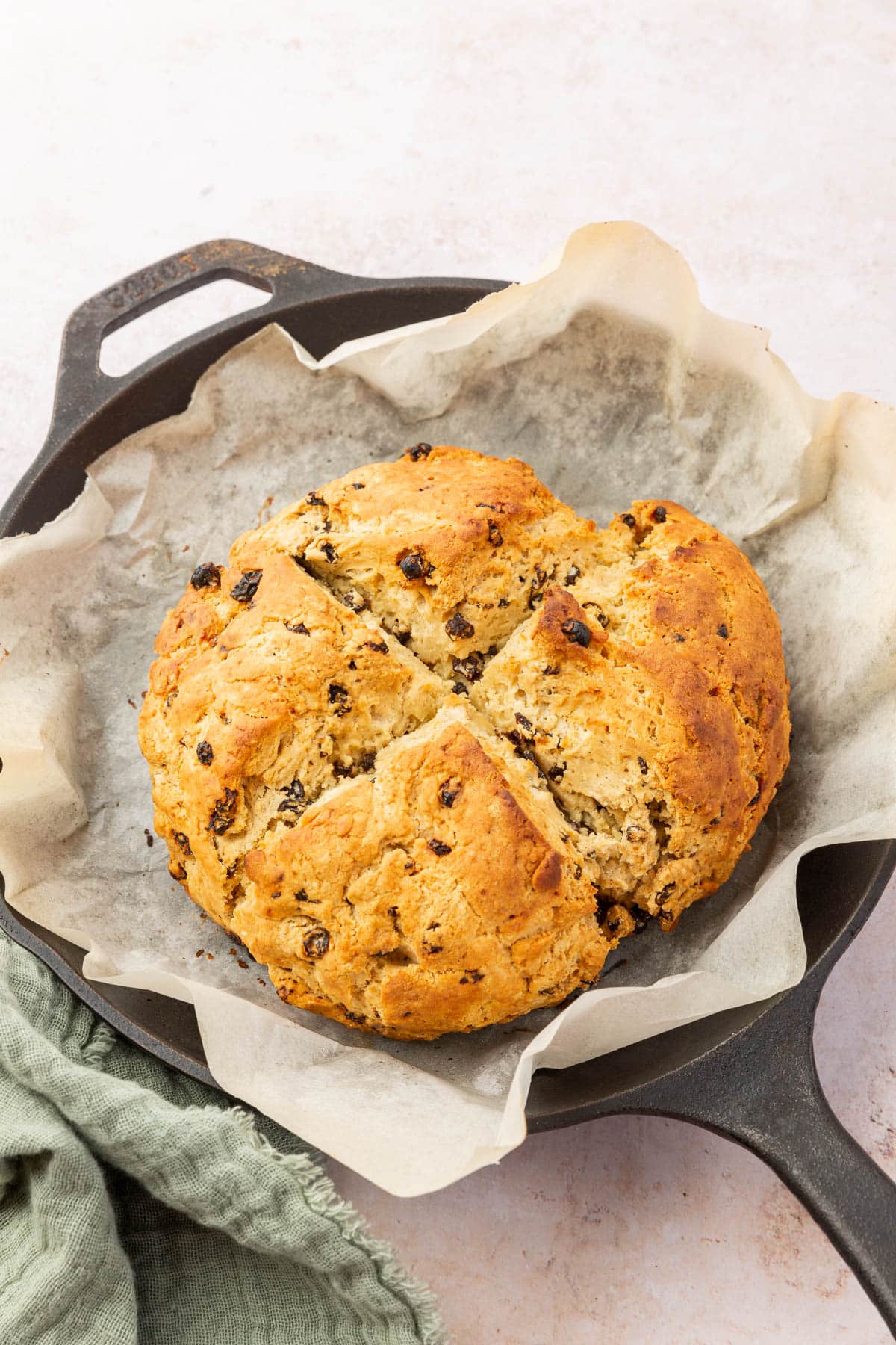 A loaf of gluten-free Irish soda bread in a cast iron skillet lined with parchment paper.