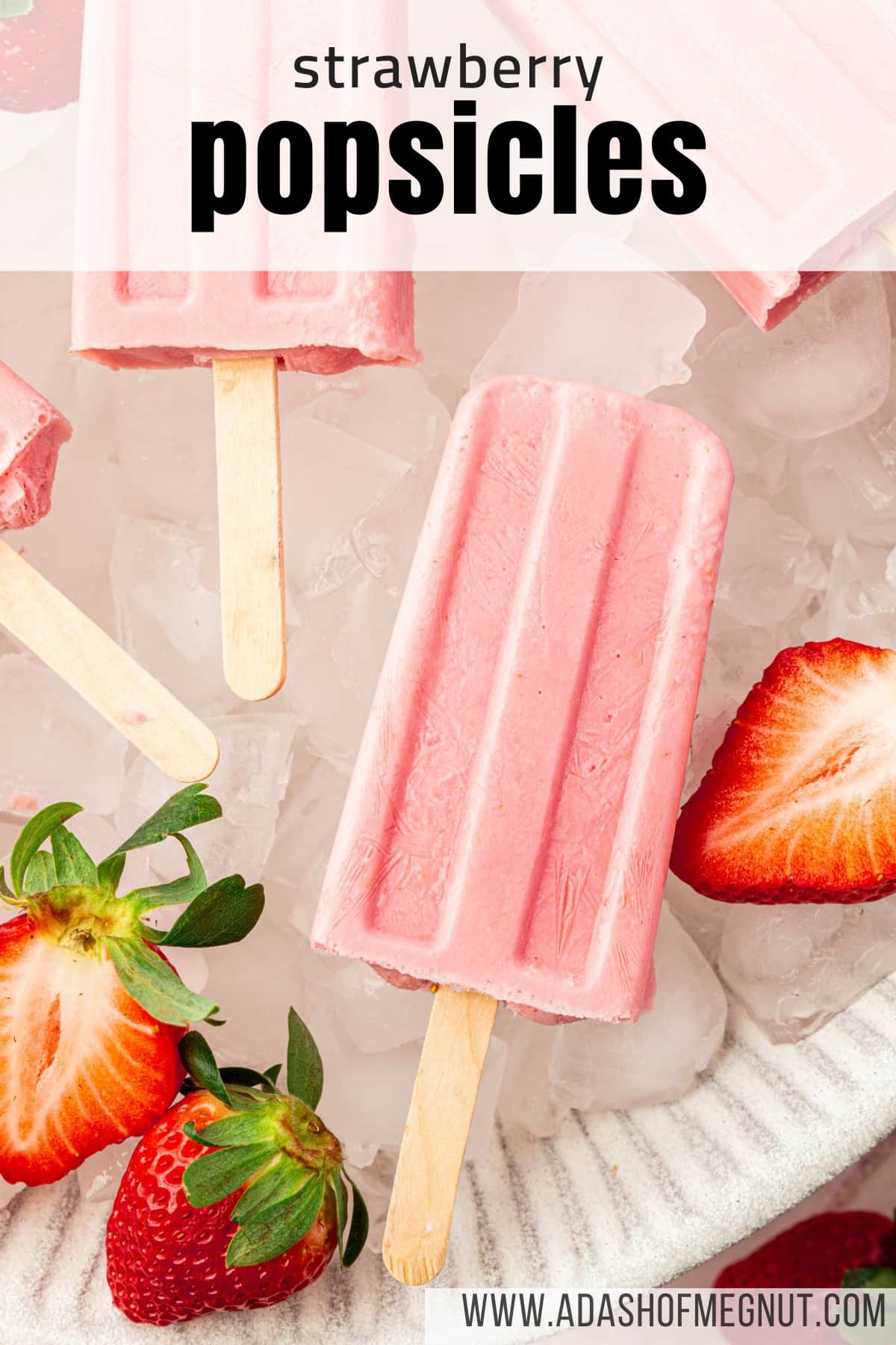 A close up of a strawberry popsicle laying in a large bowl of ice cubes with some fresh strawberry halves surrounding the popsicles.