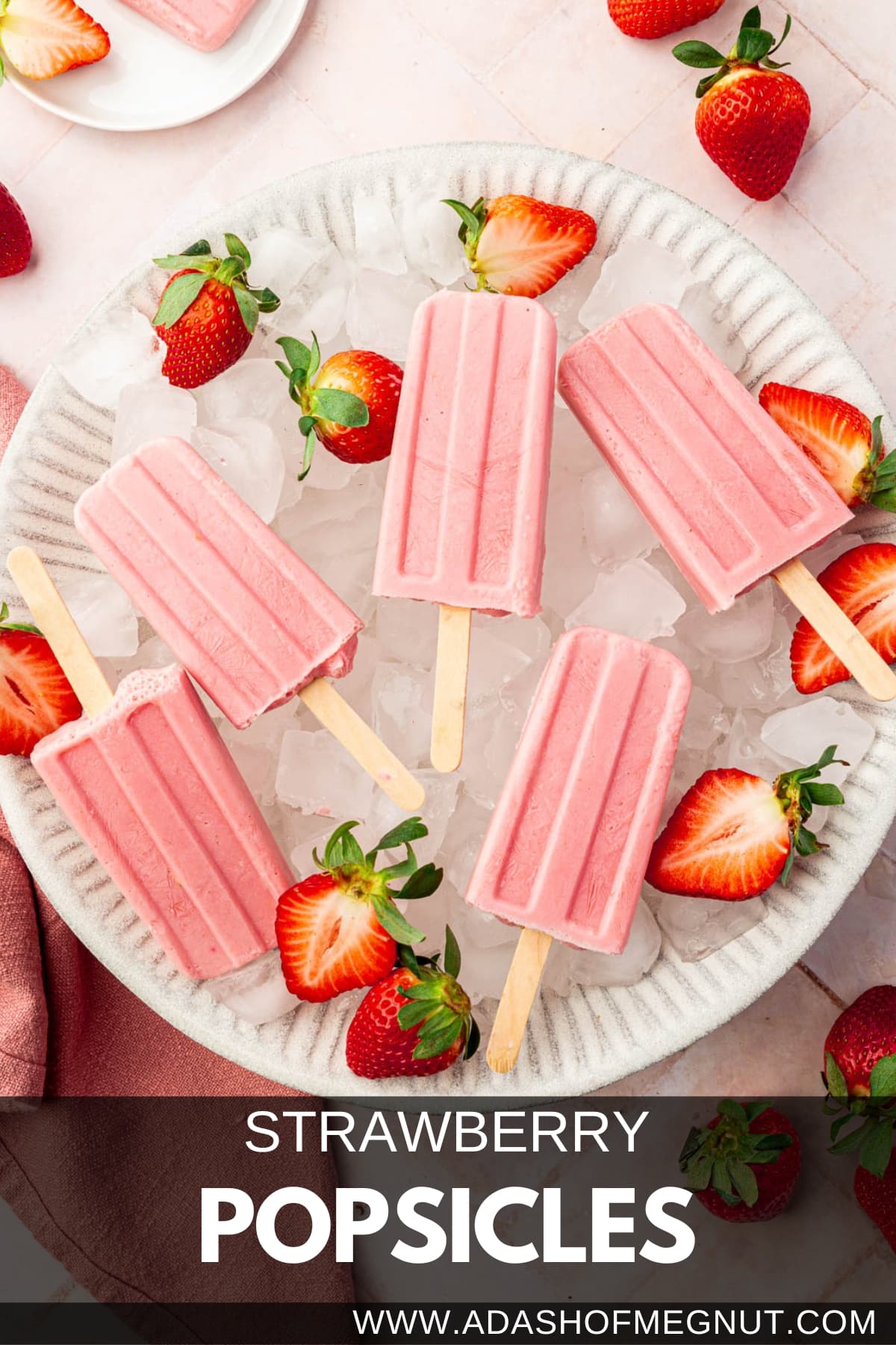 A large bowl filled with ice cubes and topped with strawberry yogurt popsicles with fresh strawberry halves surrounding the popsicles.