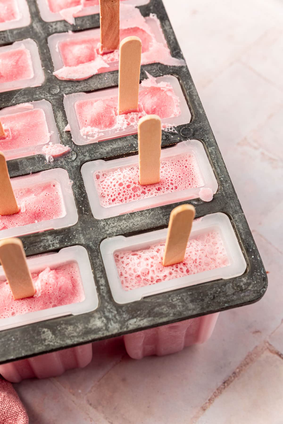 A popsicle mold tray filled with frozen strawberry popsicles with popsicle sticks in them.