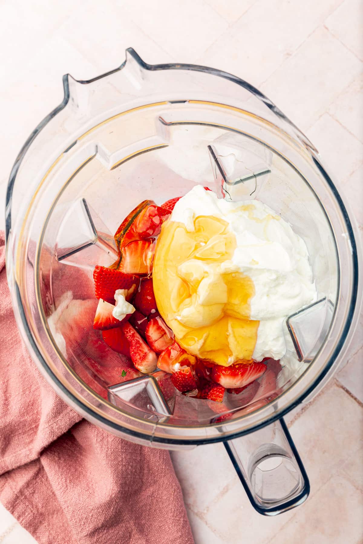 A blender will fresh strawberries, honey, and Greek yogurt in it before mixing together.