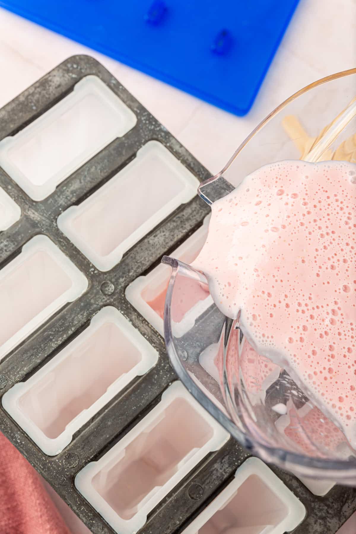A blender pouring a strawberry yogurt mixture into popsicle molds.