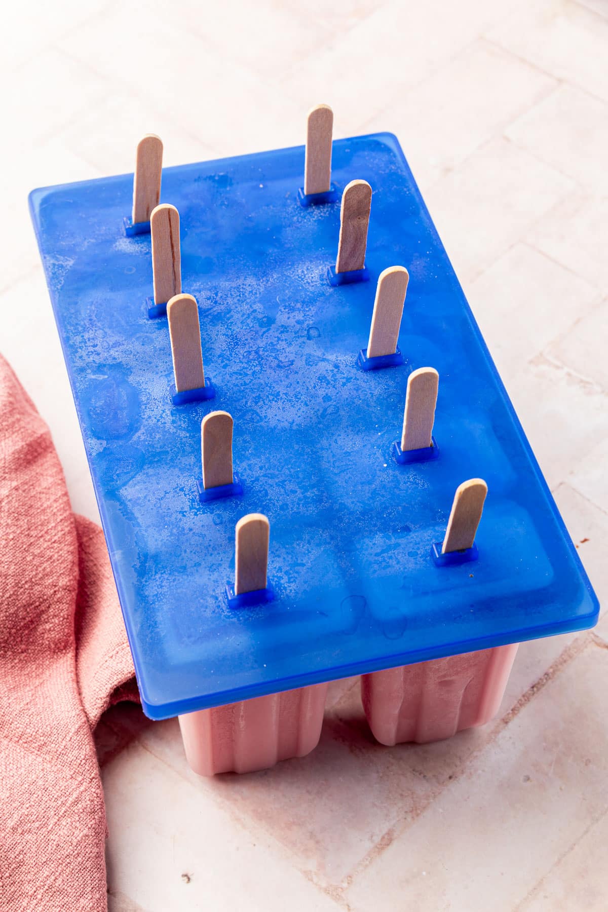 A popsicle tray filled with frozen strawberry popsicles with a blue lid in place.