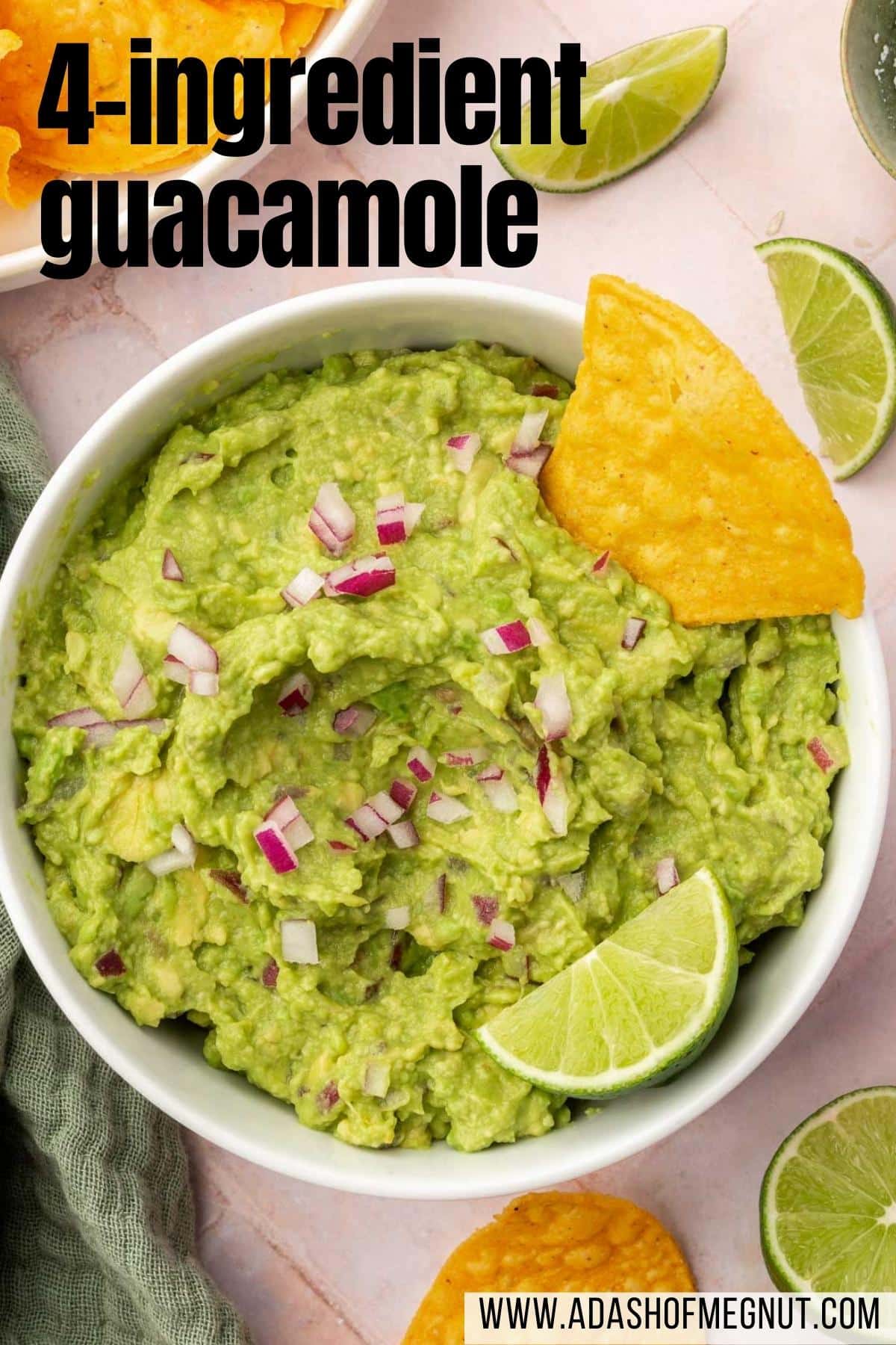 A closeup of a bowl of guacamole topped with a lime wedge, diced red onion, and a tortilla chip.