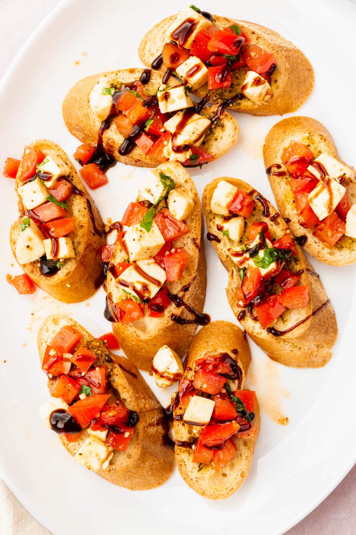 An overhead view of eight pieces of gluten free bruschetta with diced tomatoes, diced fresh mozzarella, basil and drizzle of balsamic glaze.