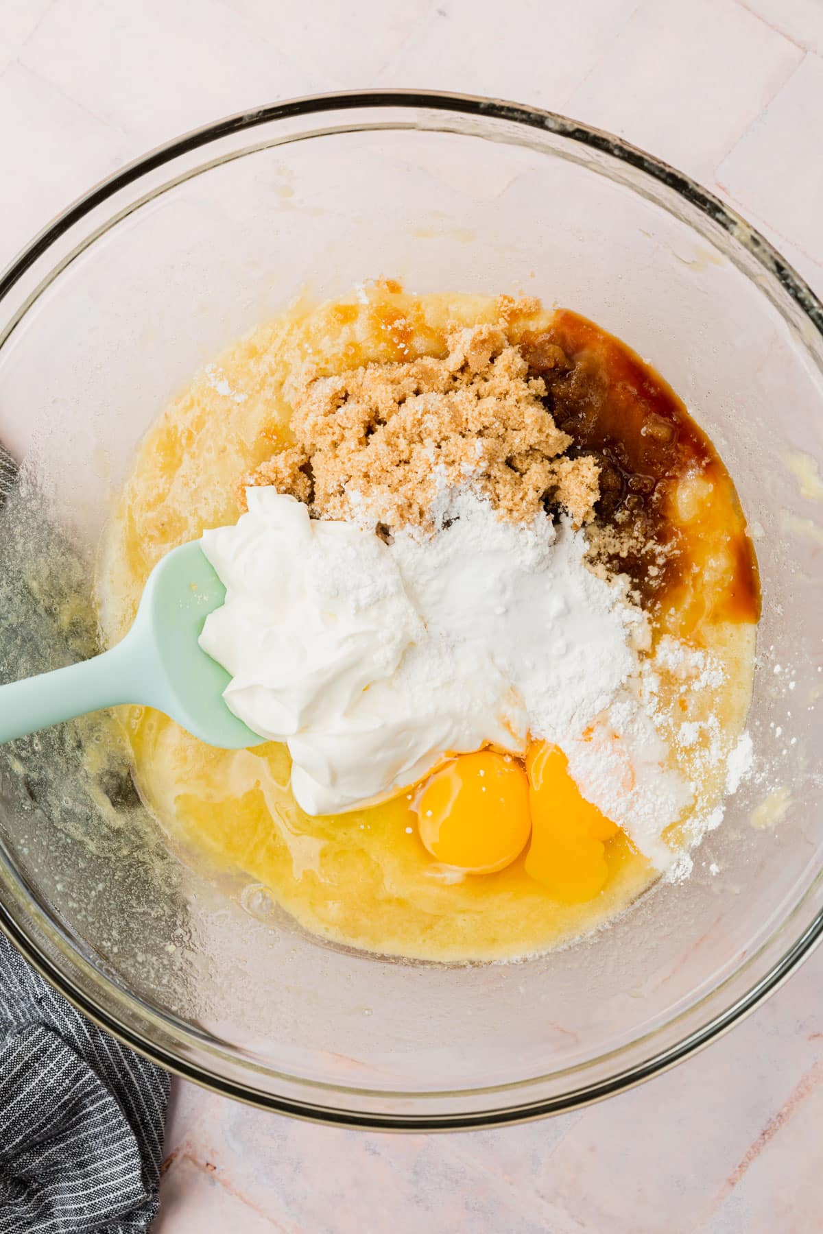 A glass mixing bowl with mashed bananas, brown sugar, sour cream, eggs, melted butter and vanilla extract in it.