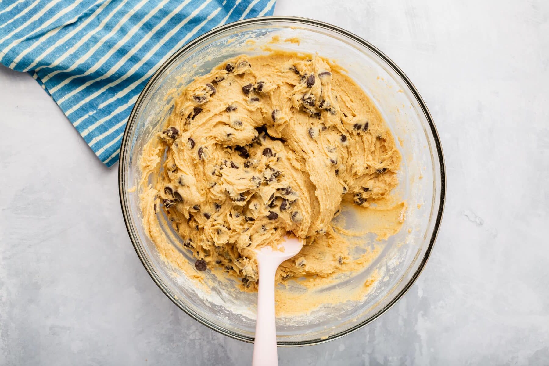 A glass mixing bowl with gluten free chocolate chip cookie bar dough in it with a pink spatula.