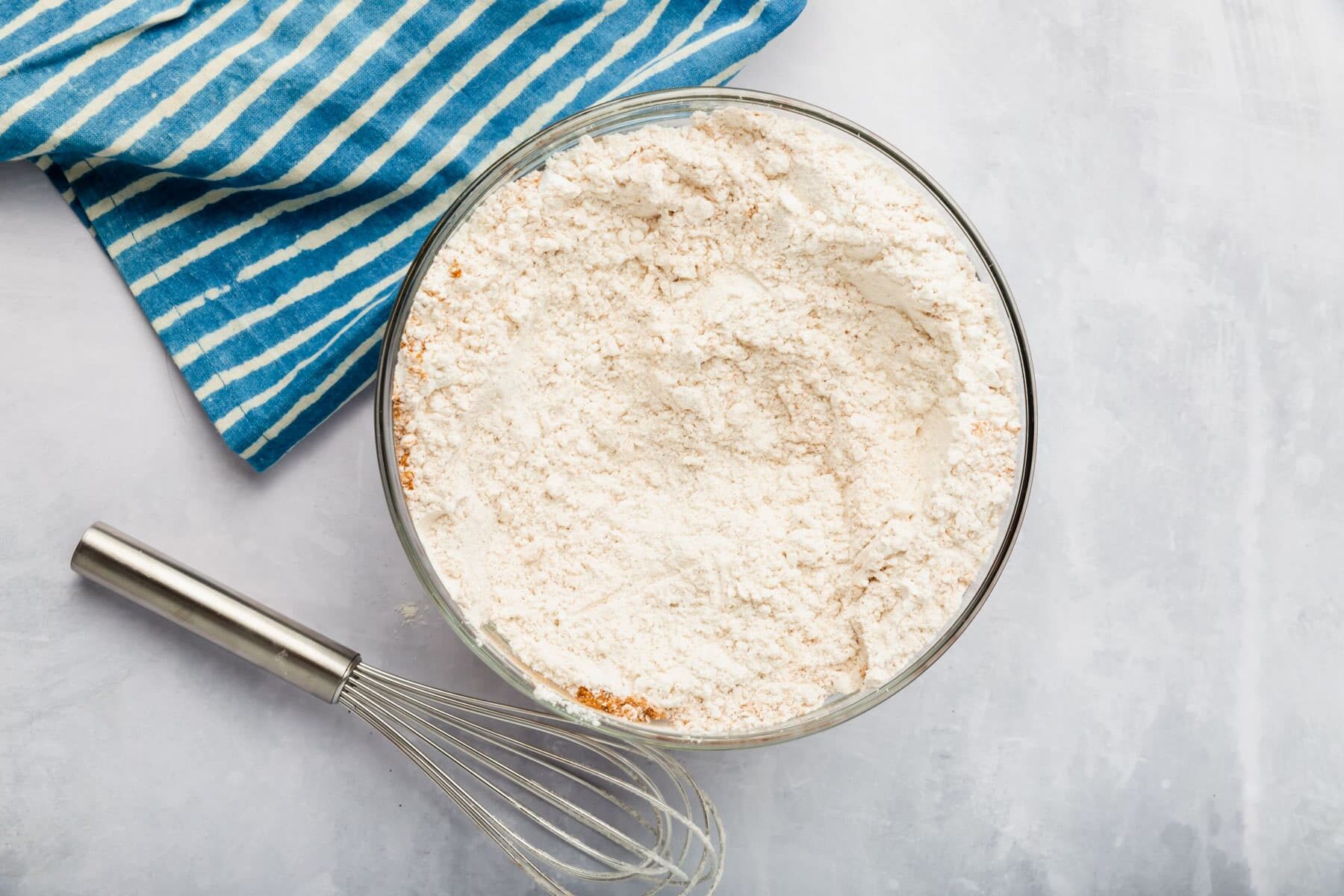 A glass mixing bowl with a gluten free flour blend in it with a whisk to the side.
