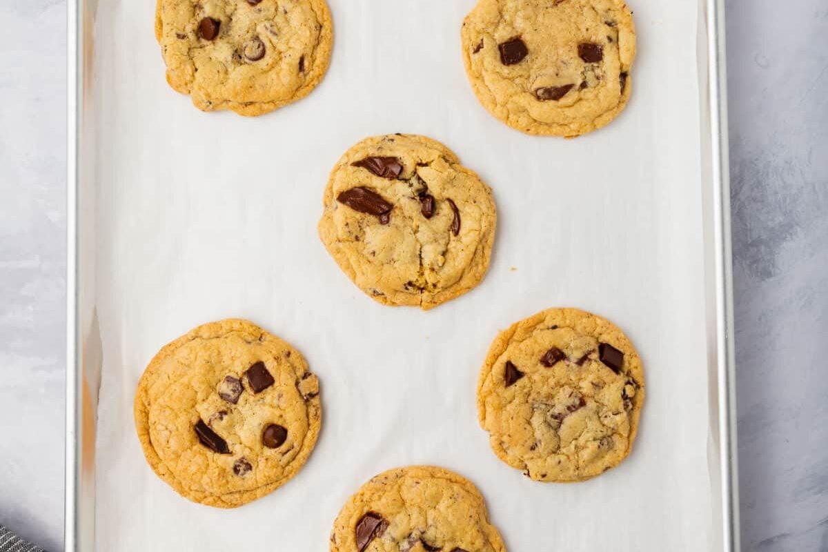 Six gluten-free chocolate chip cookies on a baking sheet lined with parchment paper.