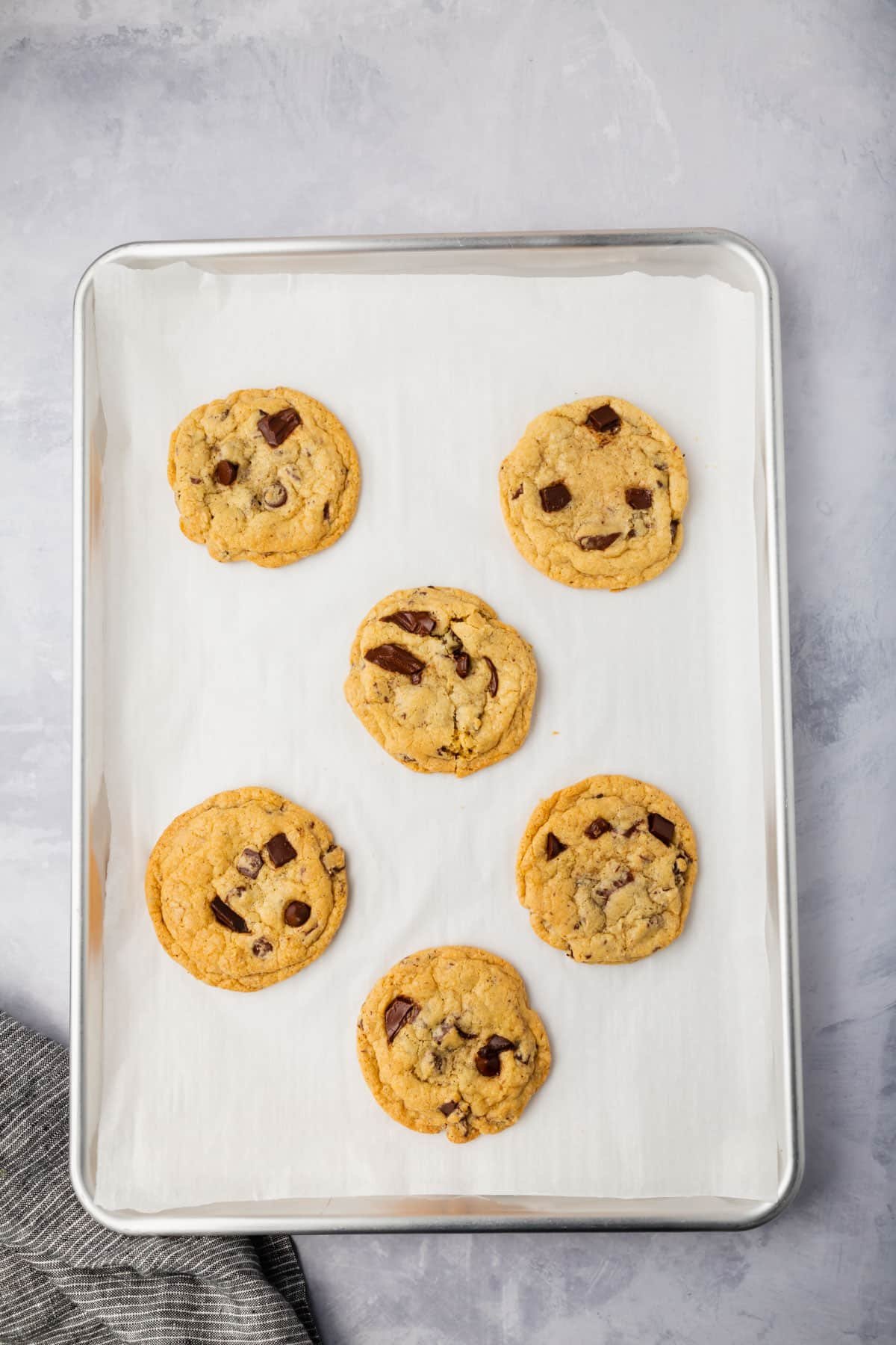 Six gluten-free chocolate chip cookies on a baking sheet lined with parchment paper.