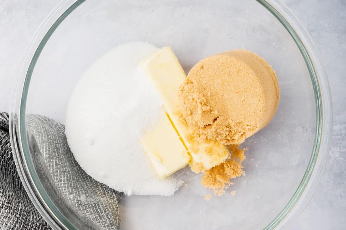 A glass mixing bowl with granulated sugar, brown sugar and softened unsalted butter in it.