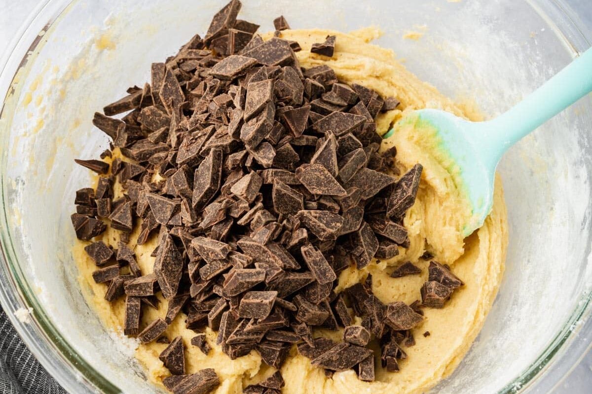 A glass mixing bowl with gluten free cookie dough topped with chocolate chunks.