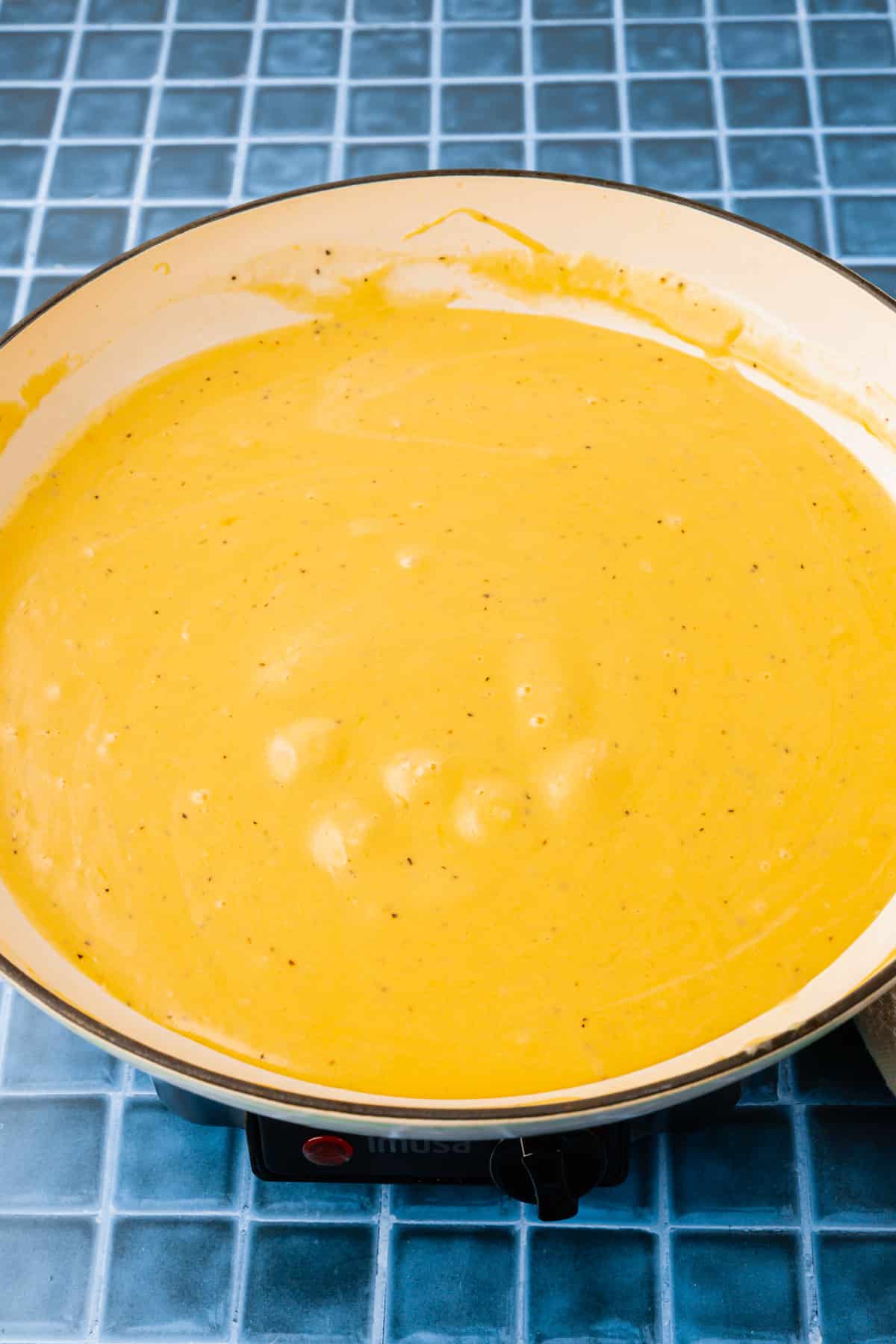 A white braising pan with a gluten-free cheese sauce in it.