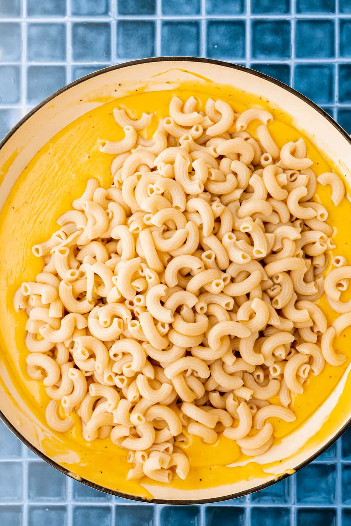 An overhead view of a skillet of gluten free macaroni pasta on top of a gluten-free cheese sauce before mixing together.