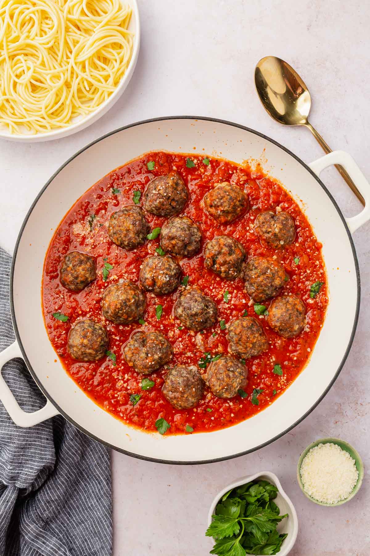 An overhead view of a braising pan with gluten-free meatballs simmering in marinara sauce with a bowl of gluten-free spaghetti to the side.