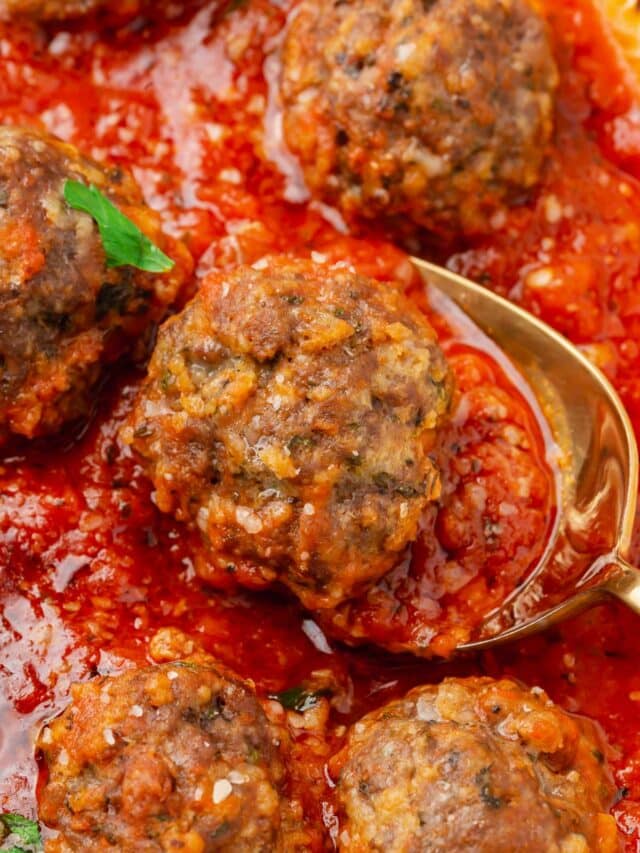 A closeup of a saucepan of gluten-free meatballs simmering in marinara sauce with a spoon under one meatball.