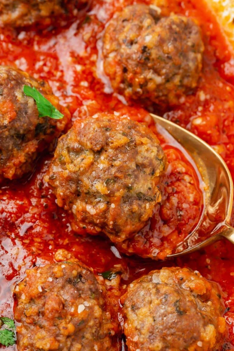 A closeup of a saucepan of gluten-free meatballs simmering in marinara sauce with a spoon under one meatball.