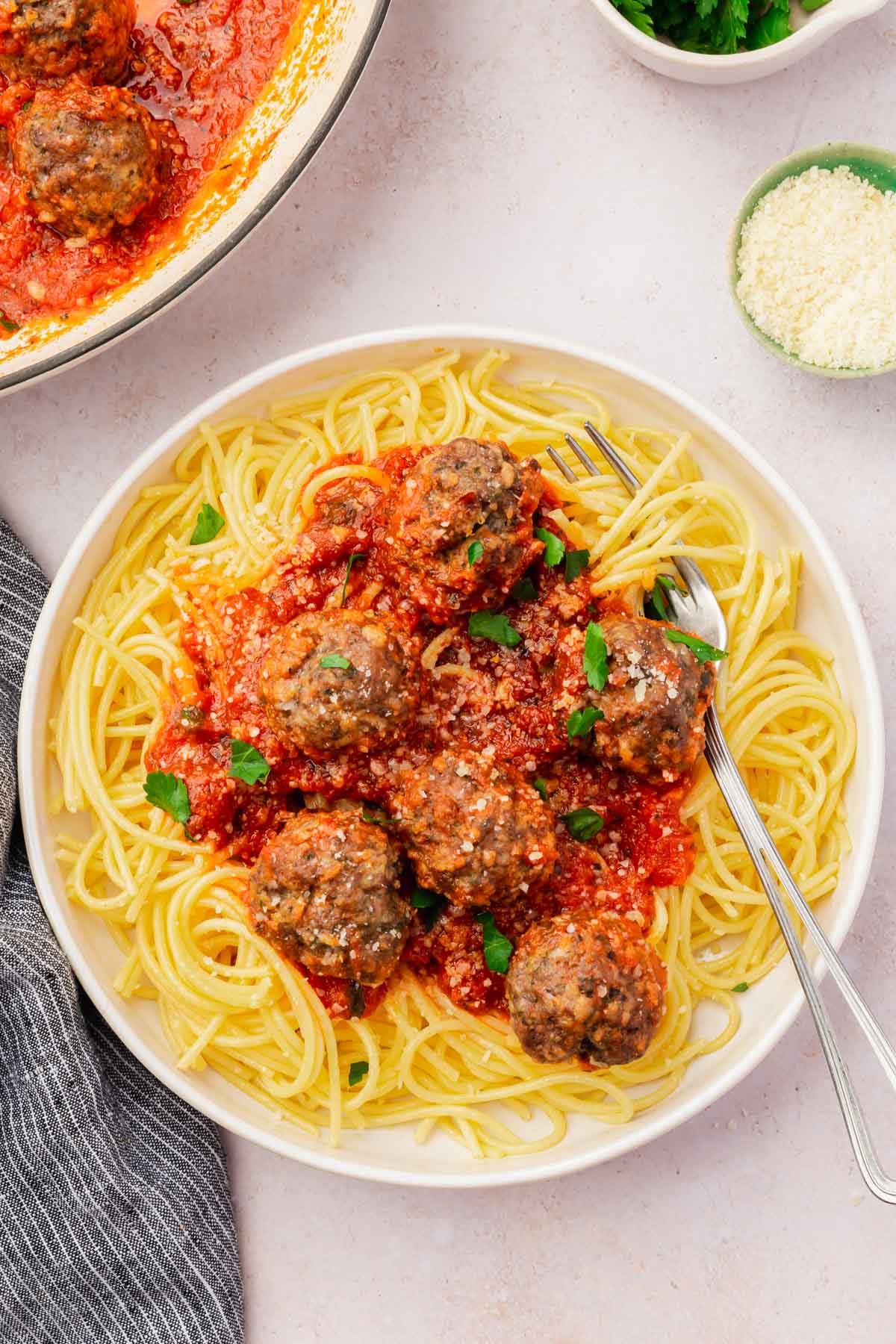 An overhead view of a bowl of gluten-free spaghetti topped with six gluten-free meatballs, marinara sauce and fresh parsley with a fork in the spaghetti.