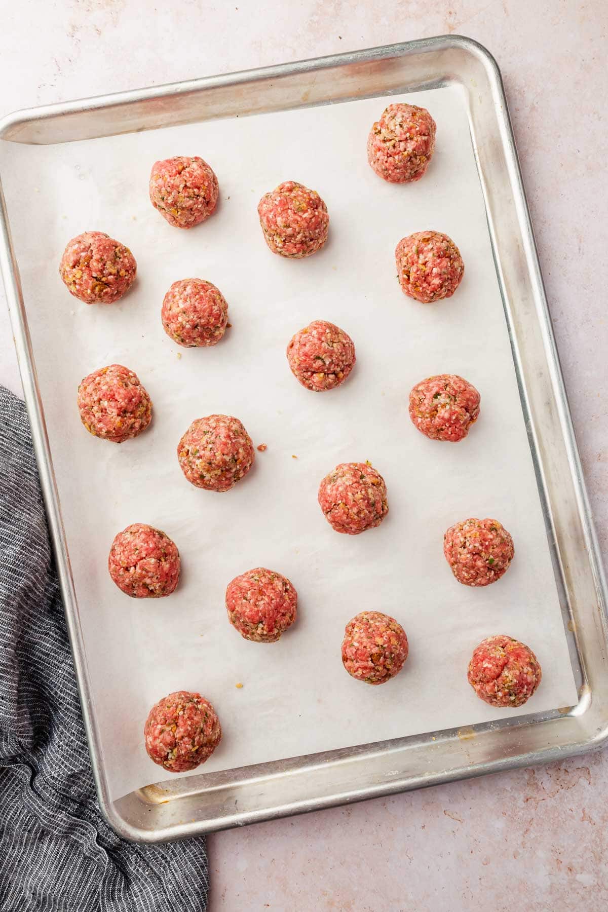 An overhead view of a parchment lined baking sheet with raw gluten free meatballs in rows.
