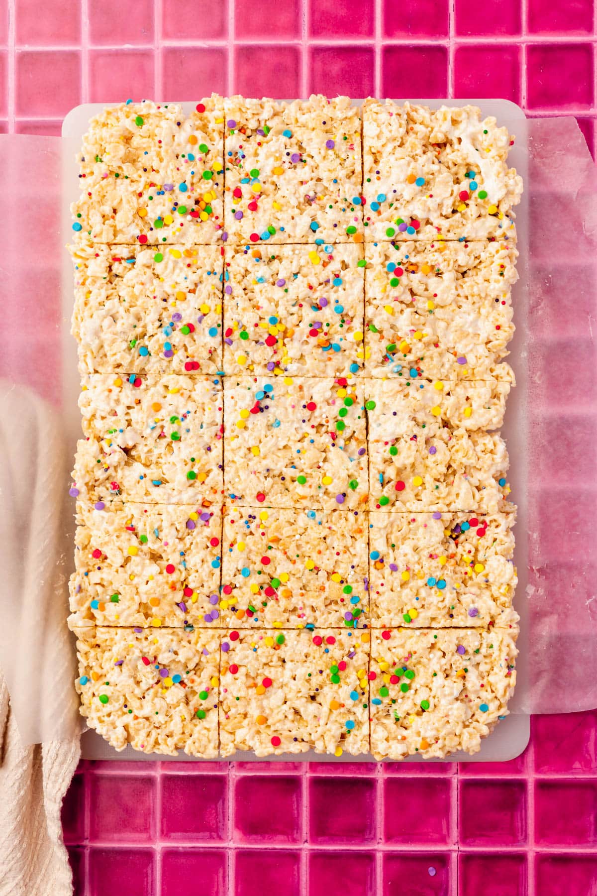 A slab of gluten-free rice krispy treats topped with rainbow sprinkles that have been cut into squares on a cutting board