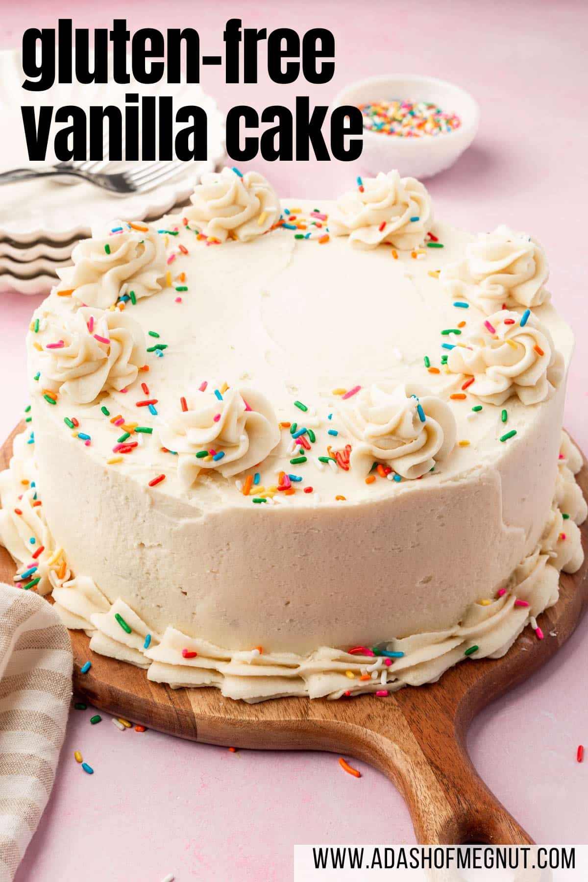 A full gluten-free vanilla cake topped with sprinkles on a wood serving board with dessert plates in the background.