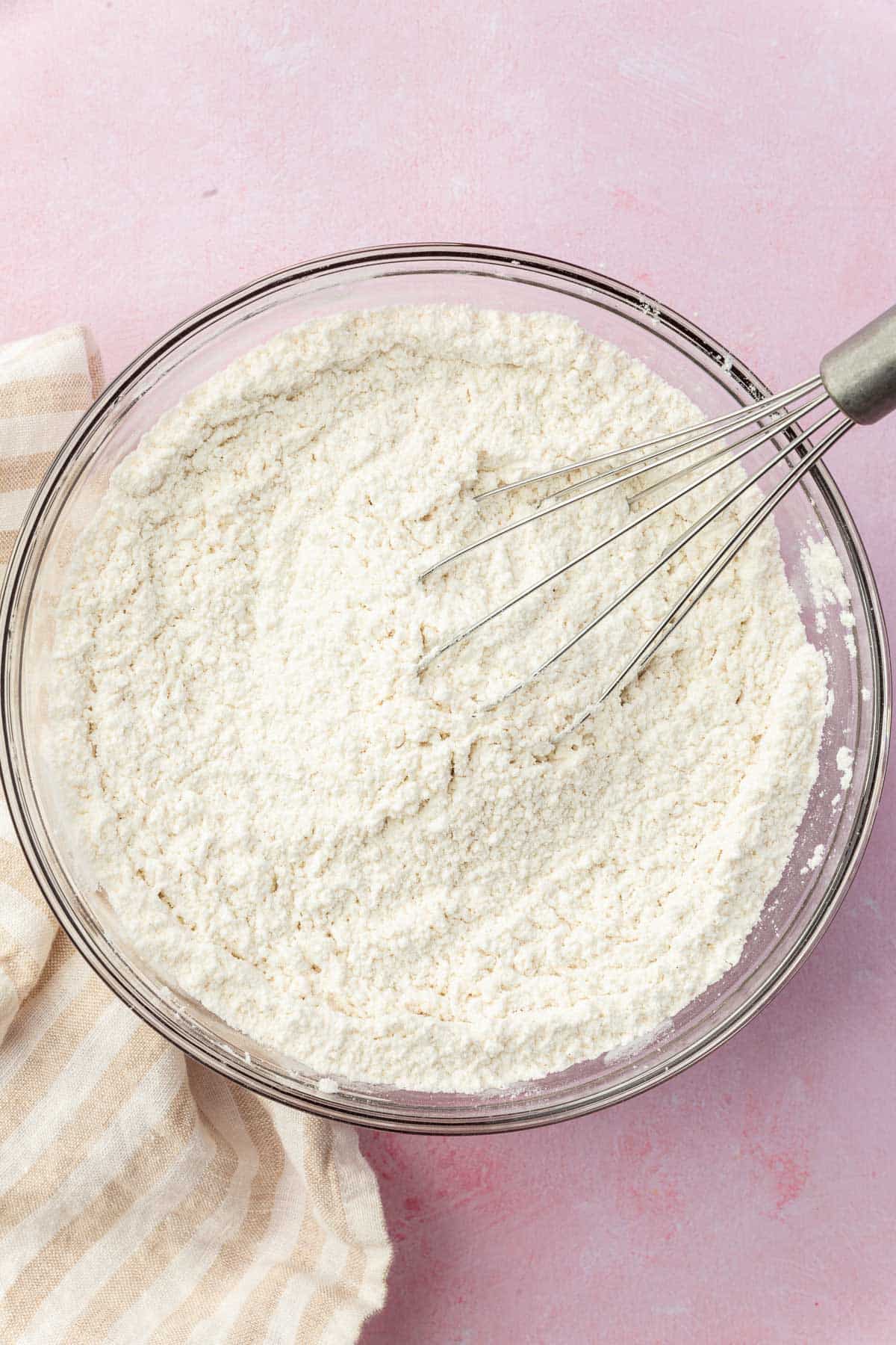 A glass mixing bowl with gluten-free and a whisk in it.