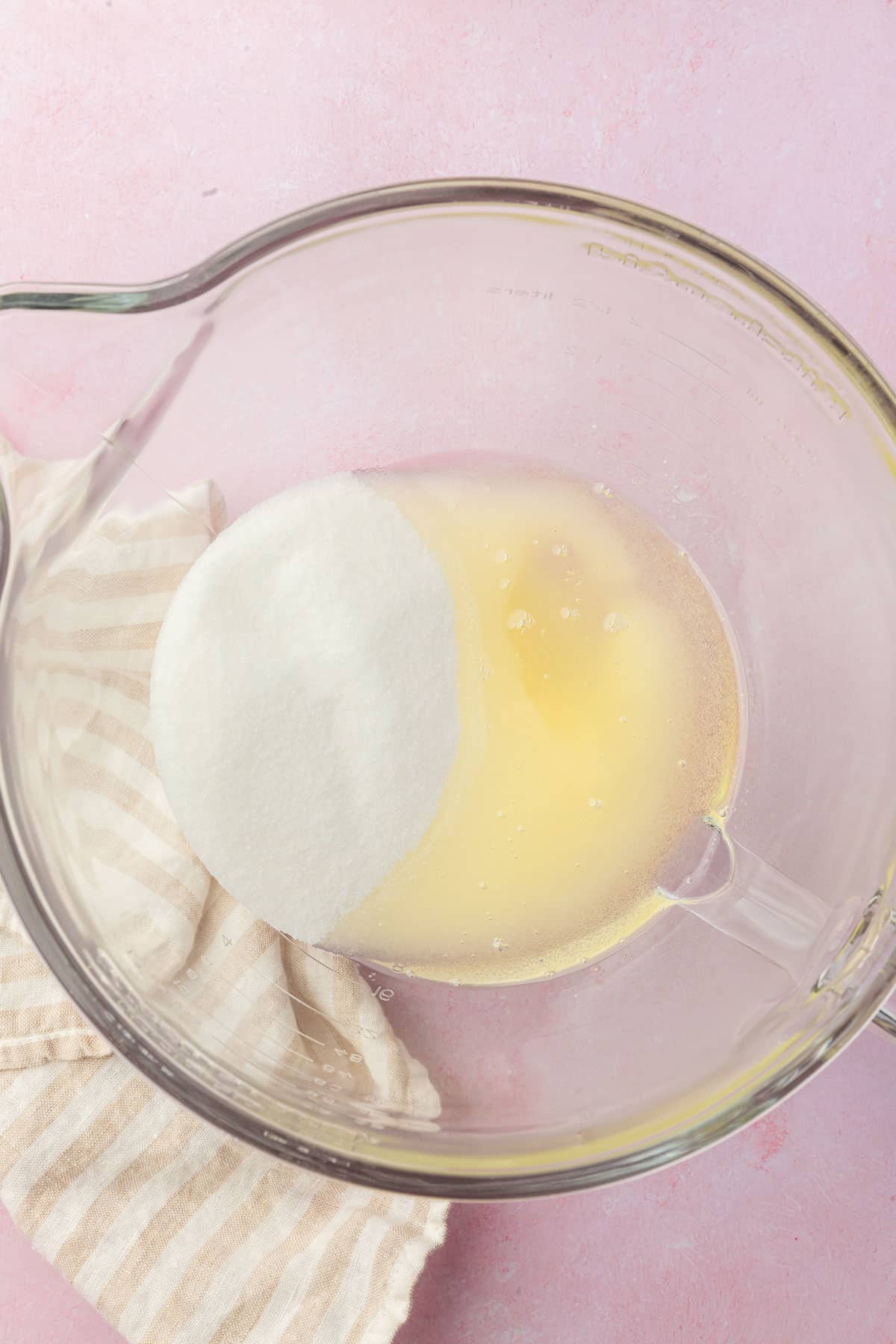 A glass mixing bowl with granulated sugar and oil in it before mixing together.