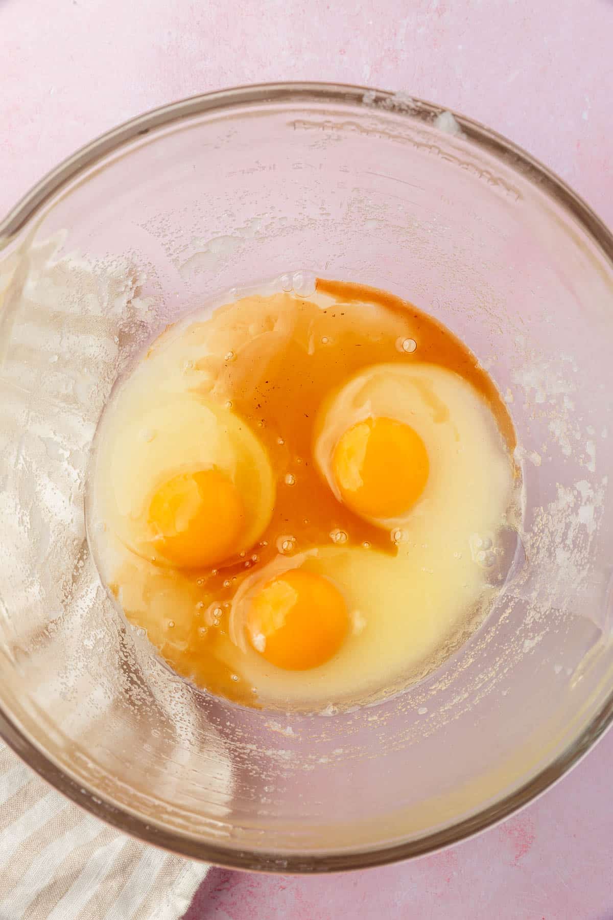 A glass mixing bowl with granulated sugar, oil, vanilla and eggs in it before mixing together.