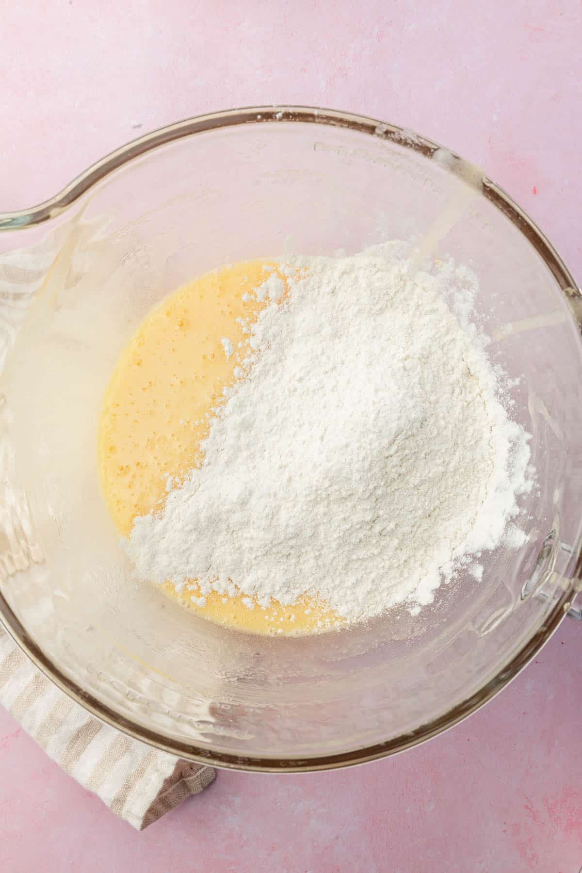 A glass mixing bowl with a cake batter in it topped with a gluten-free flour blend.