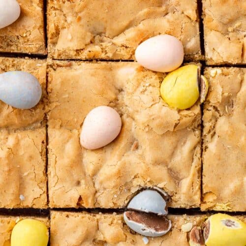 A close up shot of gluten-free blondies topped with mini chocolate eggs that have been cut into 9 equal blondies.