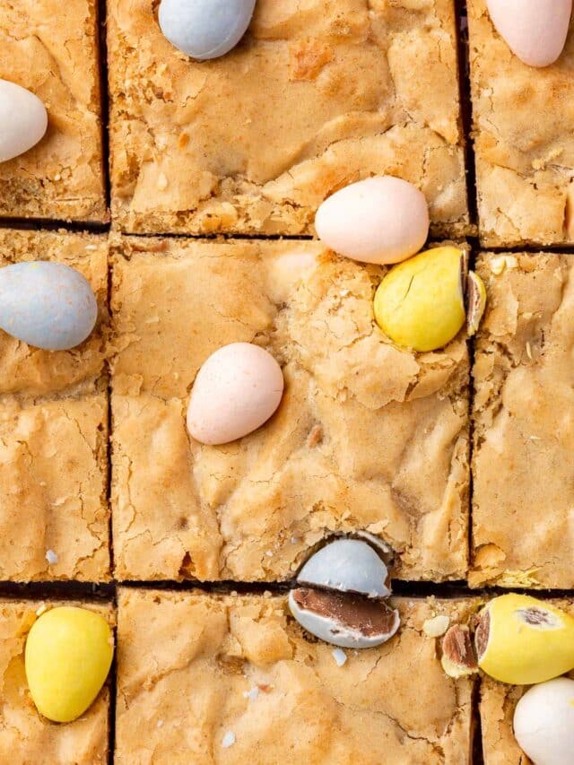 A close up shot of gluten-free blondies topped with mini chocolate eggs that have been cut into 9 equal blondies.