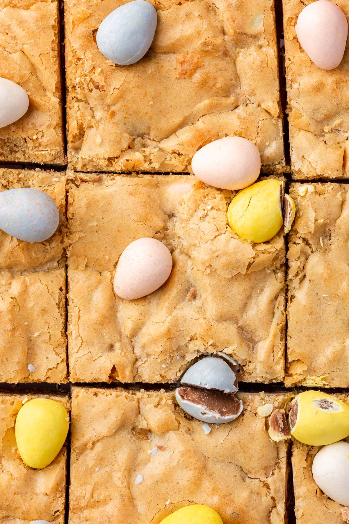 A close up shot of gluten-free blondies topped with mini chocolate eggs that have been cut into 9 equal blondies.