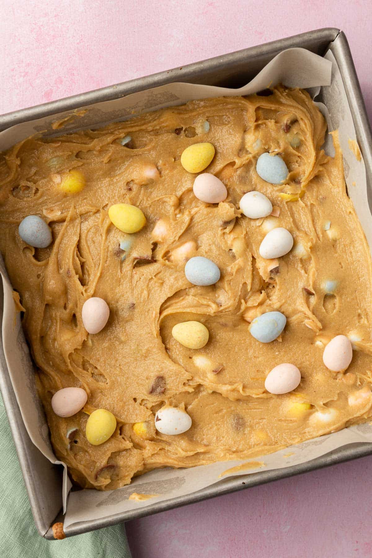 A square baking pan of gluten-free blondie batter topped with mini chocolate eggs before baking in the oven.