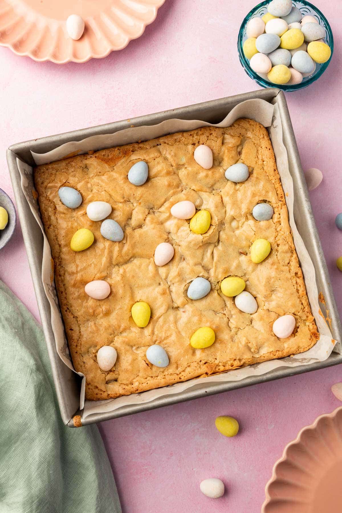 A square pan of gluten-free mini egg blondies with bowls of mini chocolate eggs to the side.