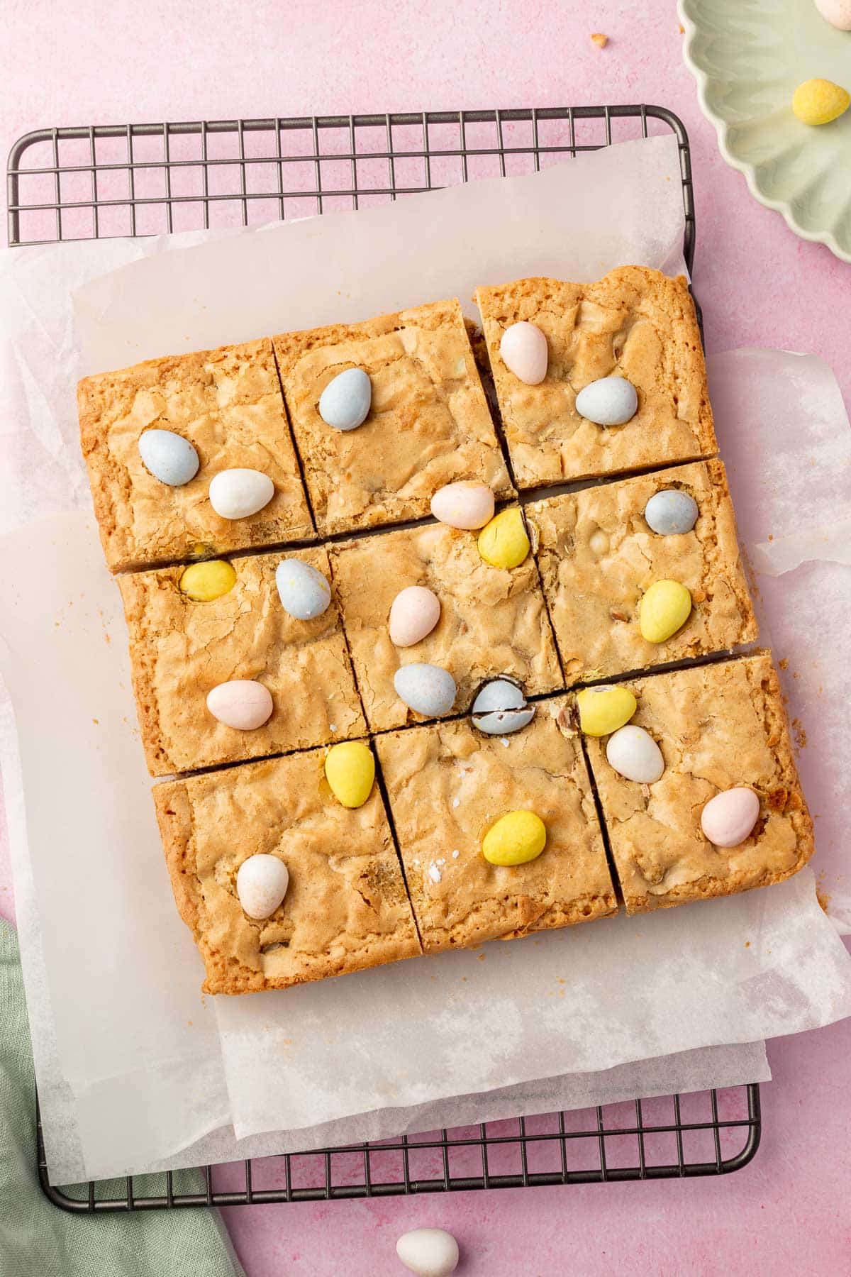 A slab of gluten-free mini egg brownies cut into 9 equal pieces on a parchment lined cooling rack.