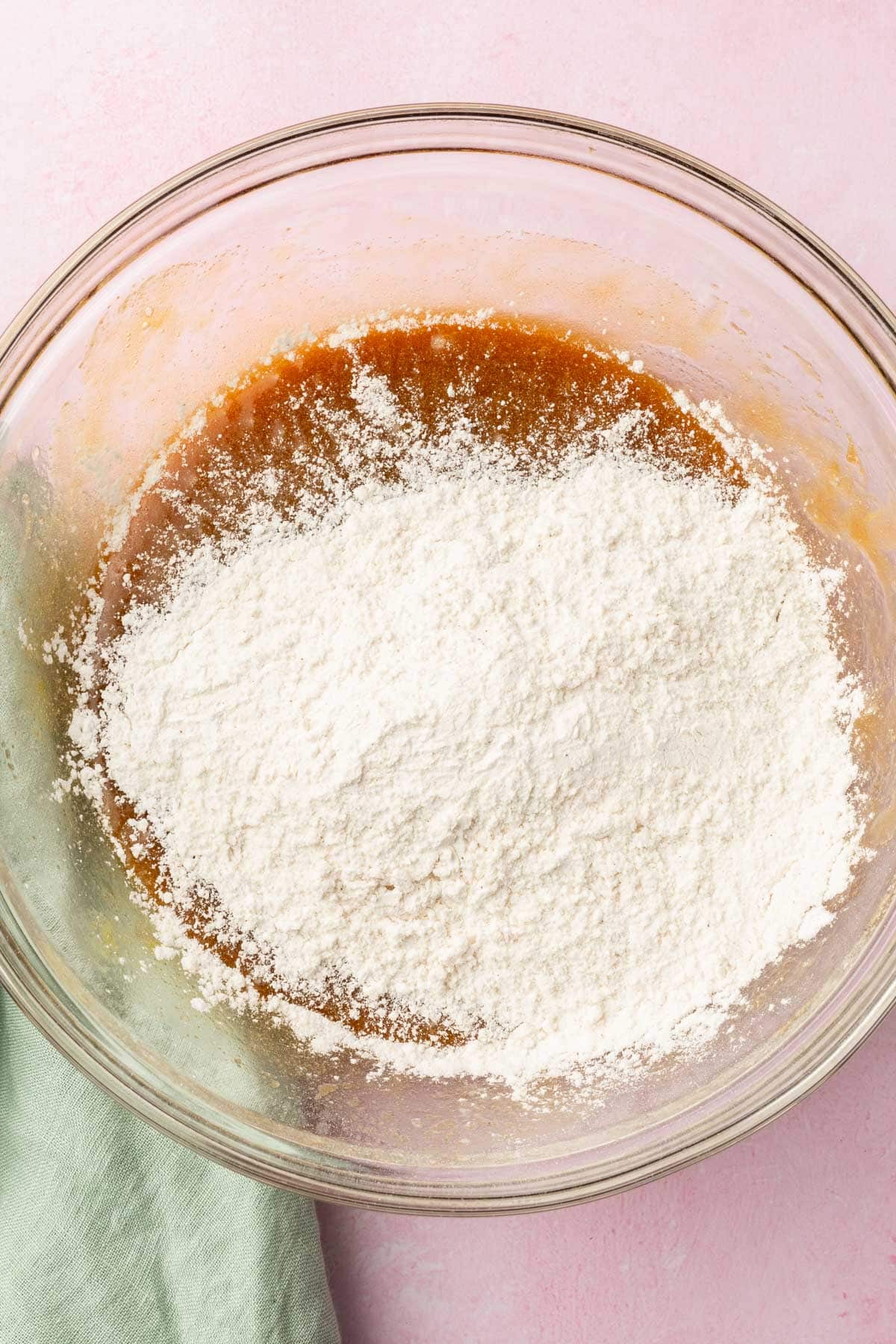 A glass mixing bowl with a brown butter and melted butter mixture topped with gluten-free flour before mixing together.