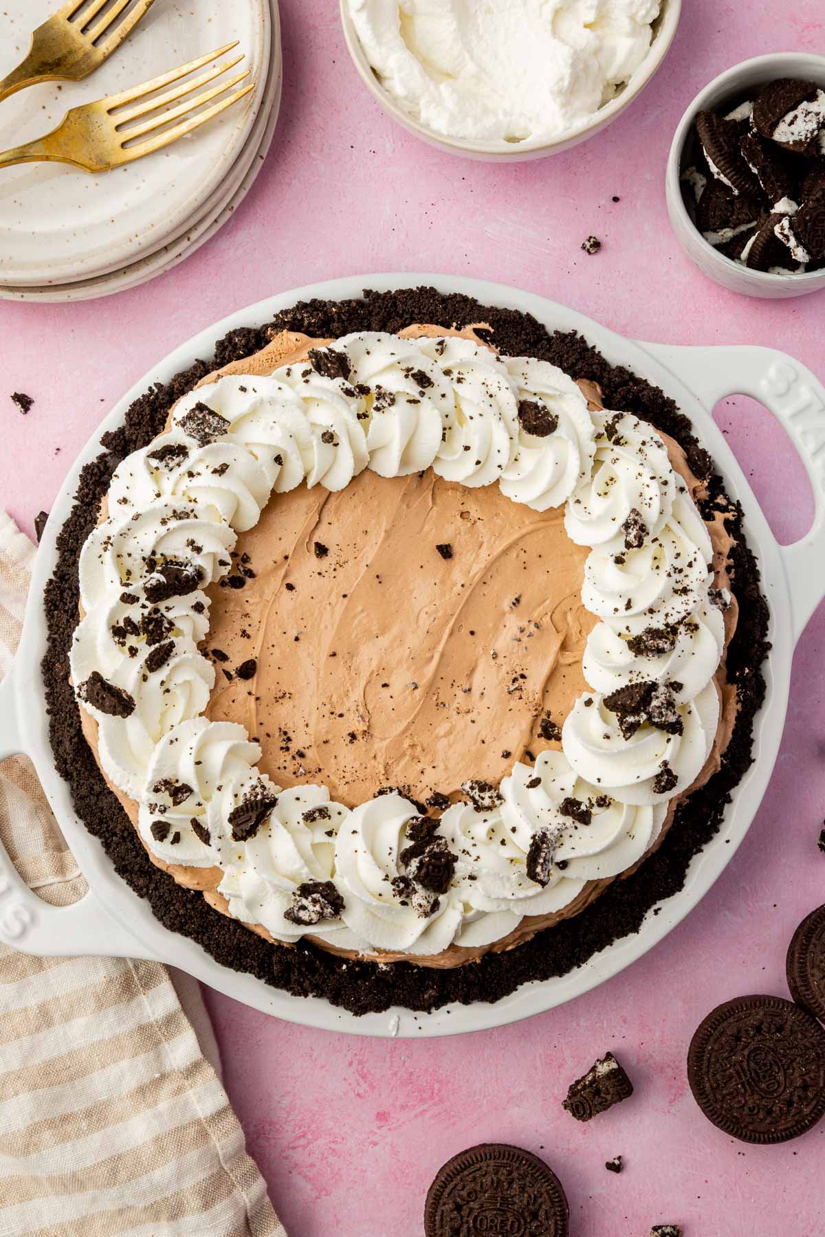 An overhead view of a gluten-free Oreo pudding pie topped with whipped cream swirls and crushed Oreos on a pink table.