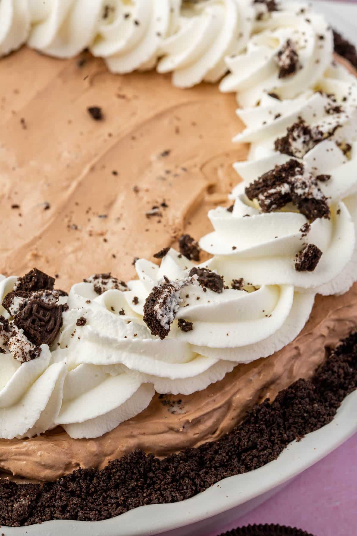 A closeup of a full gluten free Oreo mud pie topped with whipped cream swirls and crushed gluten-free Oreos.