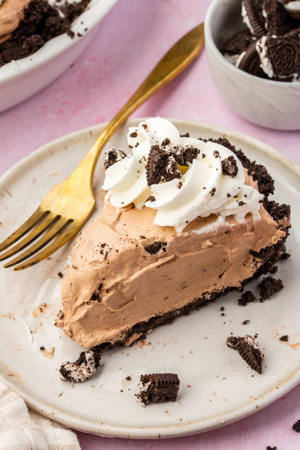 A slice of gluten-free Oreo pudding pie topped with whipped cream swirls on a dessert plate with a gold fork.