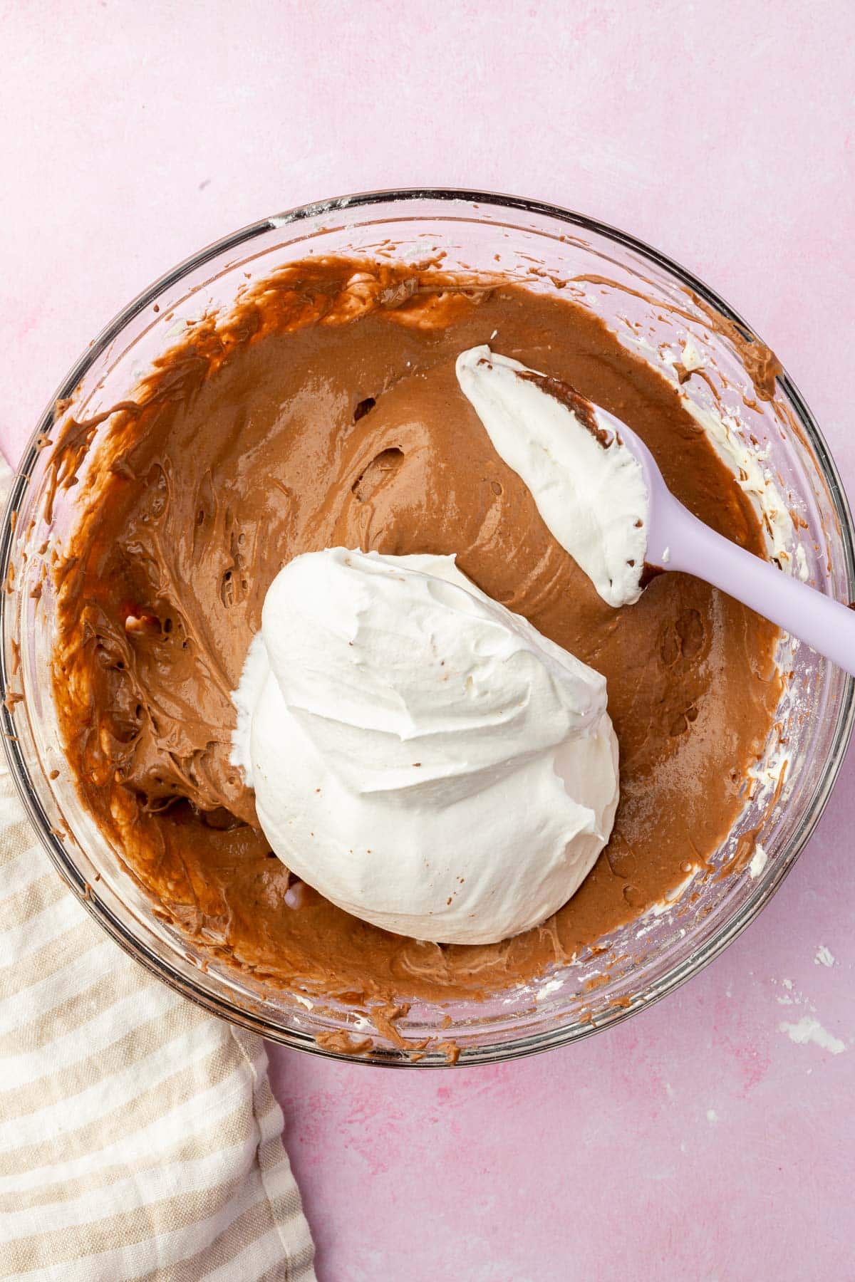A glass mixing bowl with a chocolate pudding mixture topped with a large dollop of fresh whipped cream.