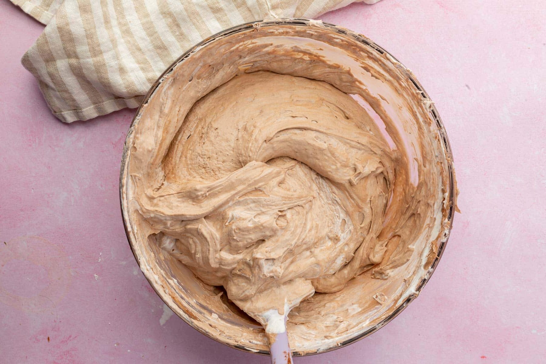 A glass mixing bowl with a whipped chocolate pudding mixture and a spatula.