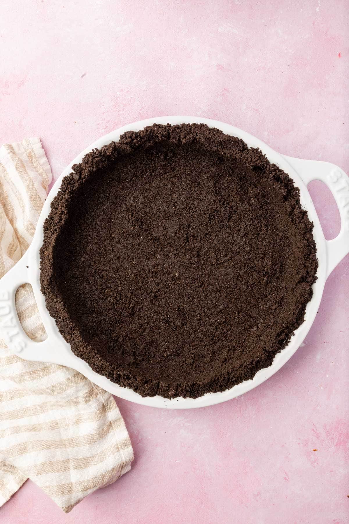 An overhead view of a gluten-free Oreo pie crust in a white pie plate on a pink table.