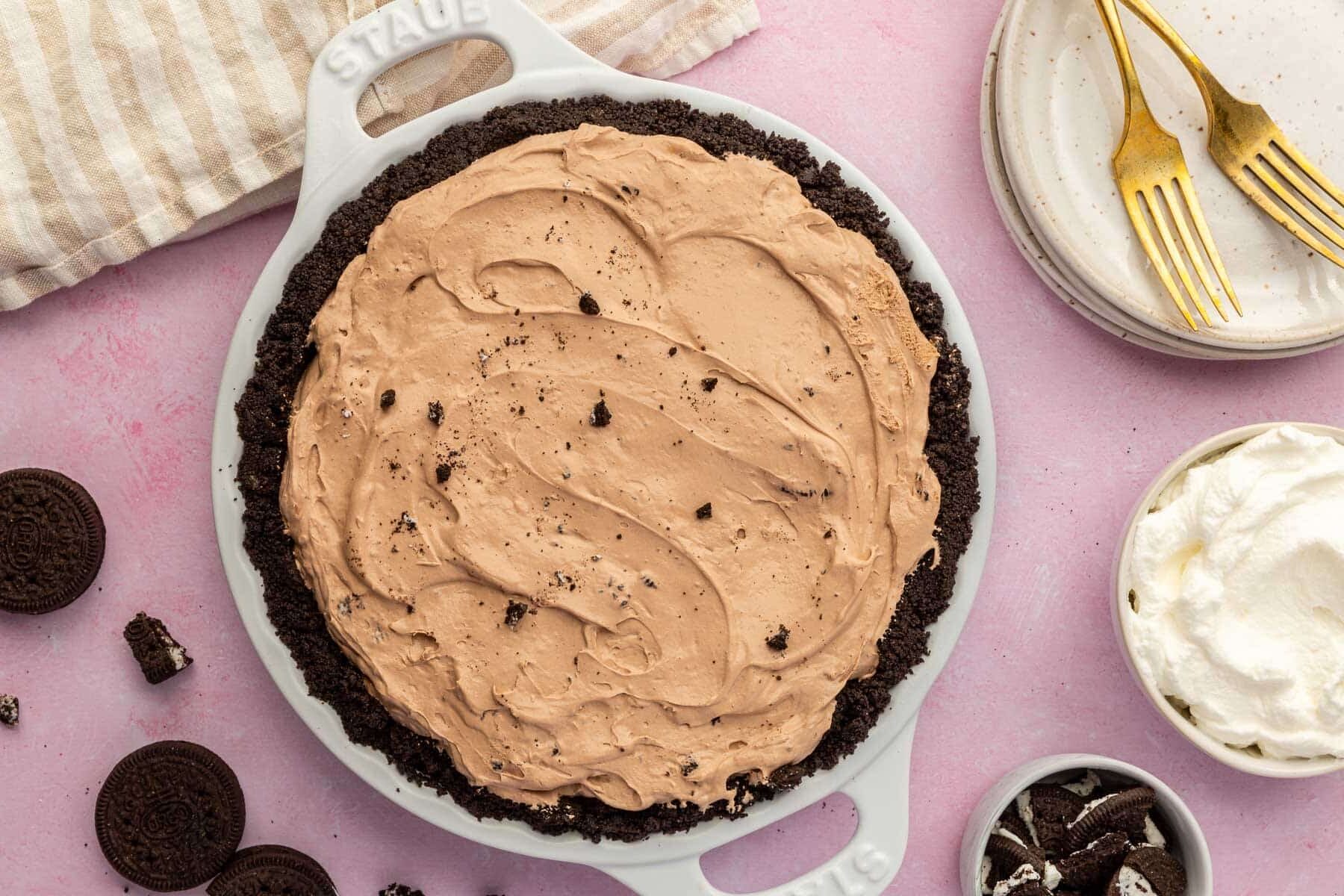 An overhead view of an Oreo pudding pie in a gluten-free Oreo pie crust on a pink table with Oreos scattered on the surface.