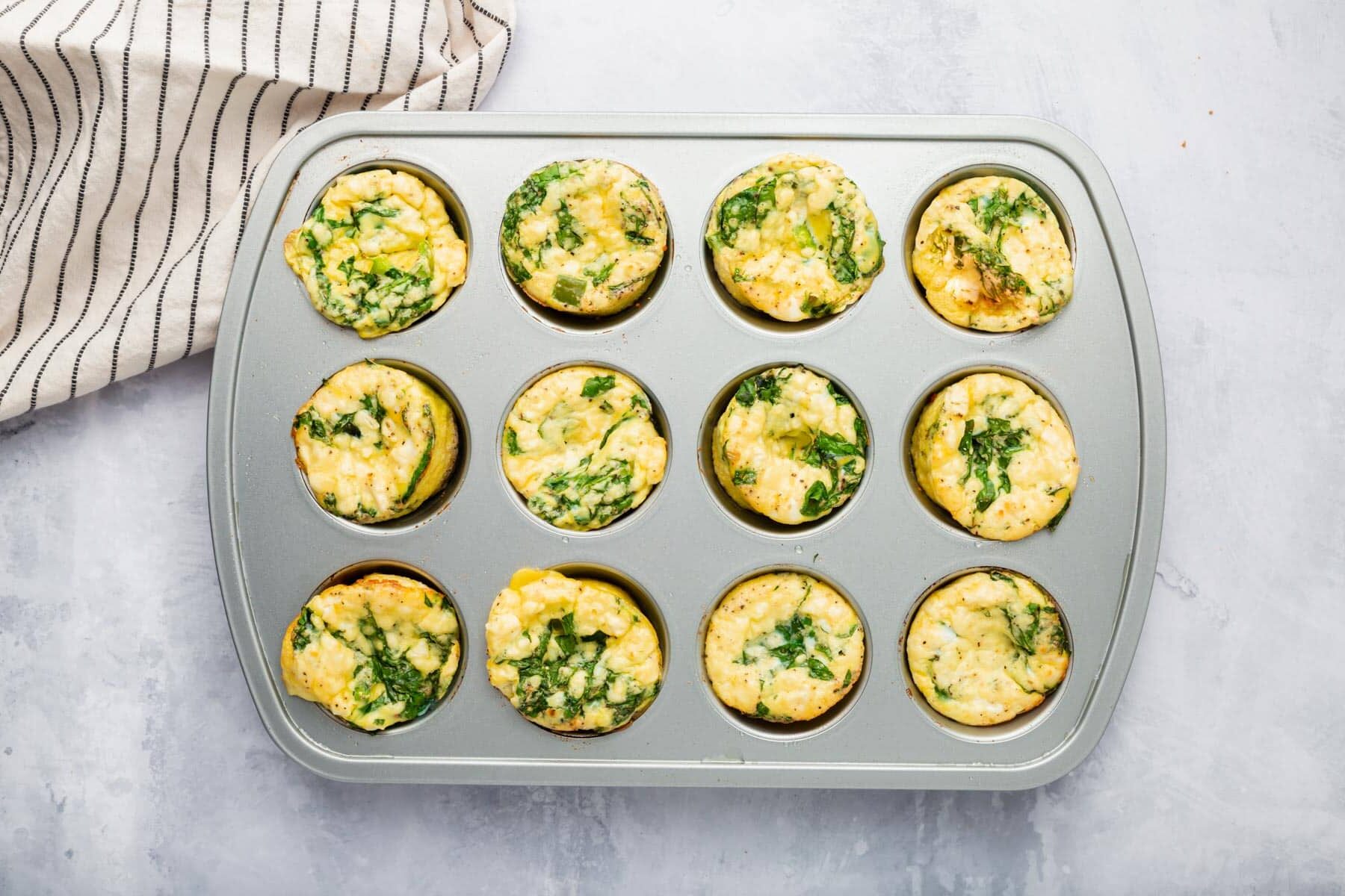 Mini spinach feta egg muffins baked in a muffin tin on a grey table.