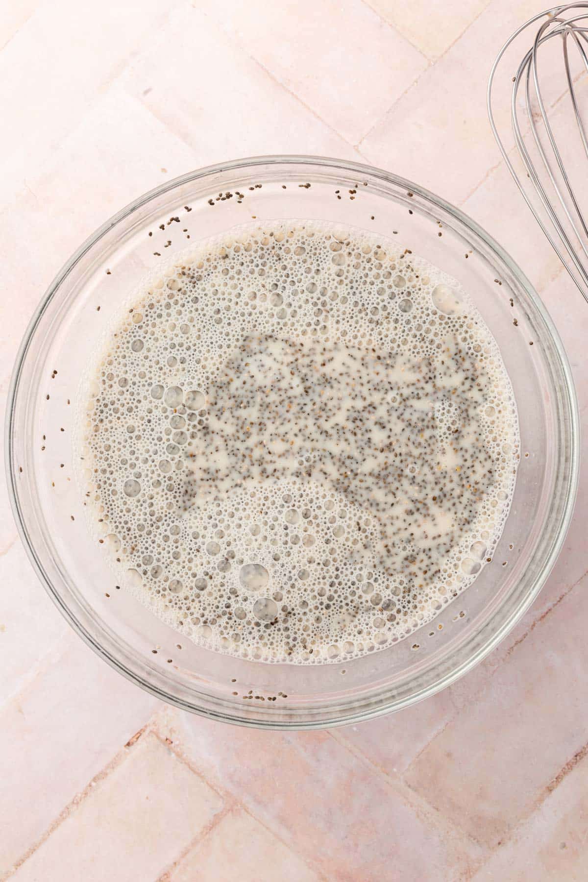 A glass mixing bowl of almond milk and chia seeds that have been whisked together before chilling in the refrigerator.